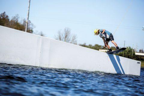 man with yellow helmet performing a kiteboard trick on a wall in the water