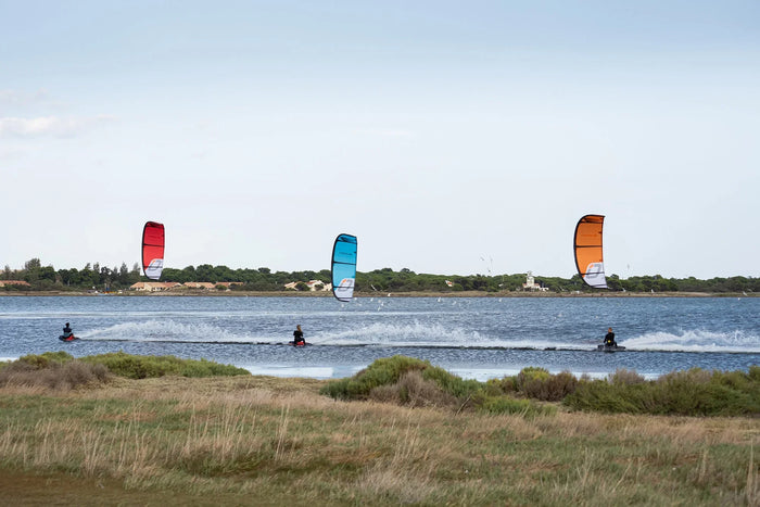 Three kiteboarders riding across flatwater with red, blue, and orange Ozone Edge V12 kites, demonstrating speed and stability in Florida conditions.