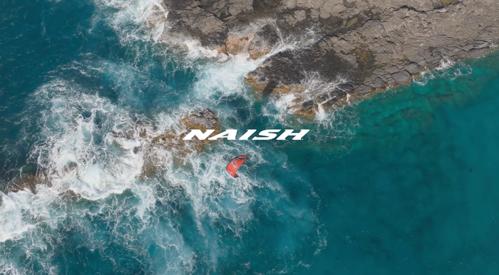 Naish brand aerial shot over ocean waves with kiteboarder riding below