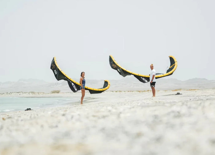 Two kiteboarders standing on a sandy beach holding Core XR PRO 2 kites, preparing to launch in light coastal wind conditions.