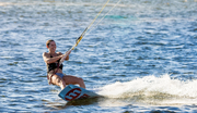 smiling woman holding onto handlebar kiteboarding in the water